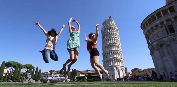 Students jumping in front of The Leaning Tower of Pisa surrounded by beautiful blue sky.